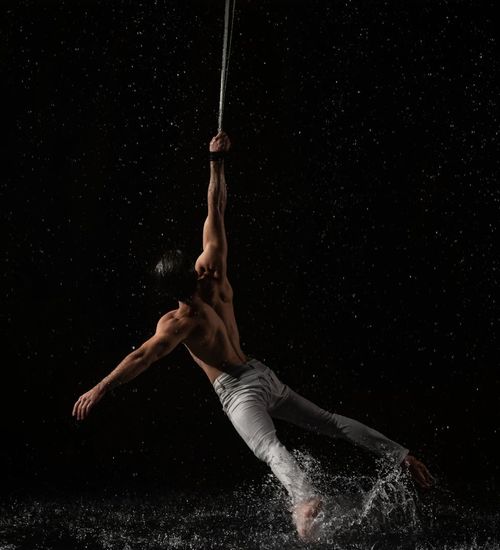 Man performing a controlled strength exercise in a dark studio.